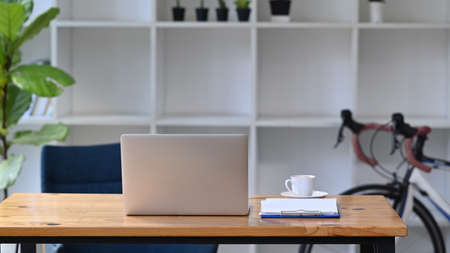 Mock up computer laptop on wooden table with bicycle in home office.の写真素材