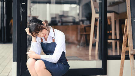 Stressed small business entrepreneur sitting in front of her coffee shop.の写真素材