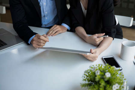 Two business people sitting each other on office desk and discussing their project.