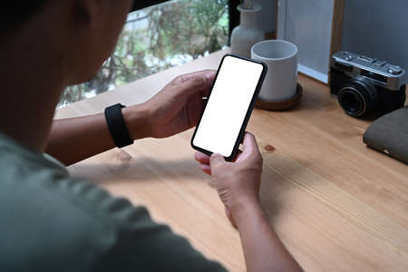 Over shoulder view of young man holding smart phone with white screen.