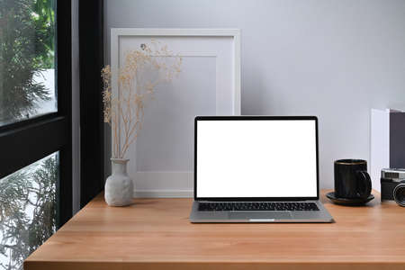 Computer laptop, books, coffee cup and picture frame on wooden table.