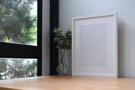 White photo frame and potted plant on wooden table near window.