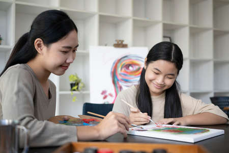 Smiling female teacher helping little girl painting picture in art class.の写真素材