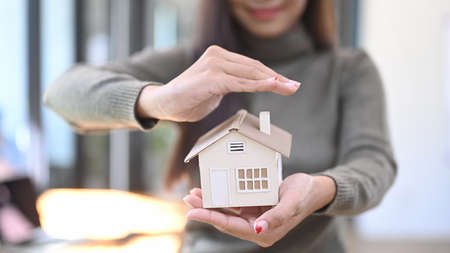 Smiling woman holding small house model. Real estate and property insurance concepts.の写真素材