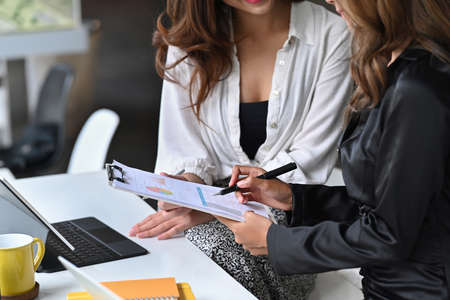 Cropped shot businesswoman holding notebook and using laptop computer at office desk.の写真素材