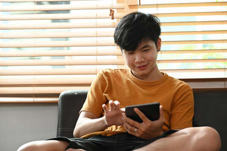 Side view smiling casual man sitting in living room and using smart phone.