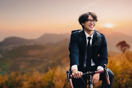 Smiling businessman standing with bicycle on road with beautiful mountains landscape background.の写真素材