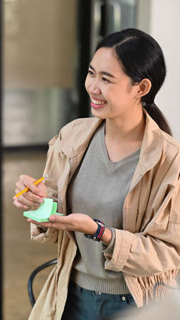 Cheerful female designer writing new ideas on sticky notes.