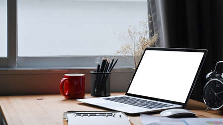 Mock up computer laptop with empty display, coffee cup and pencil holder on wooden table.