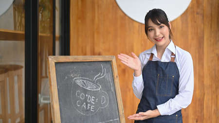 Friendly waiter standing with black board at the doorway of coffee shop.の写真素材