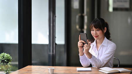 Cheerful businesswoman using smart phone while sitting at her office desk.の写真素材