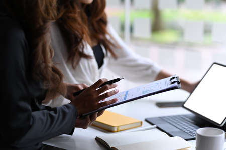 Two young businesswomen analyzing business at a on computer tablet together.