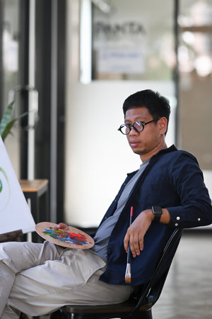 Portrait asian man artist sitting in front of canvas and looking at camera.の写真素材