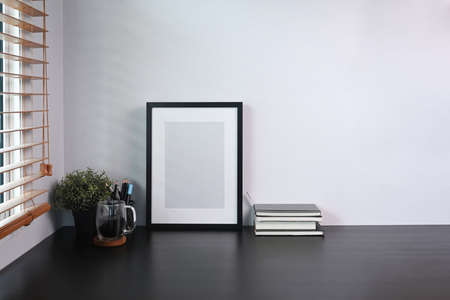 Photo frame, books, coffee cup and houseplant on black table in home office.