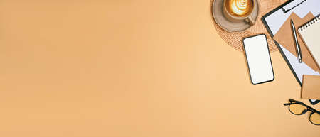 Top view mobile phone with blank screen, Coffe cup and notebooks on beige background.の写真素材