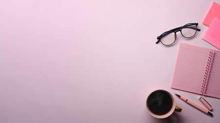 Above view coffee cup, notebook, sticky notes and glasses on pink background.