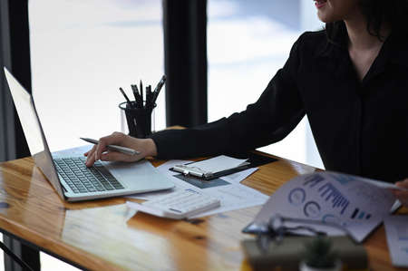 Cropped shot businesswoman using laptop computer and analyzing financial documents.の写真素材