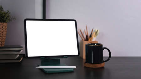 Mock up digital tablet with blank screen and coffee cup on black wooden table.