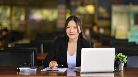 Beautiful businesswoman sitting at her workplace and smiling to camera.の写真素材
