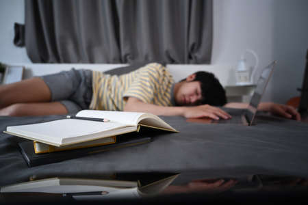 Asian man lying on the bed and study online with laptop computer.の写真素材