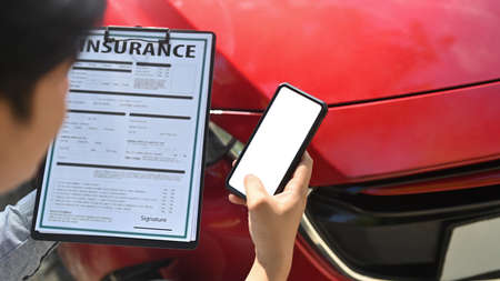 Insurance agent using smart phone while examining car after accident.の写真素材