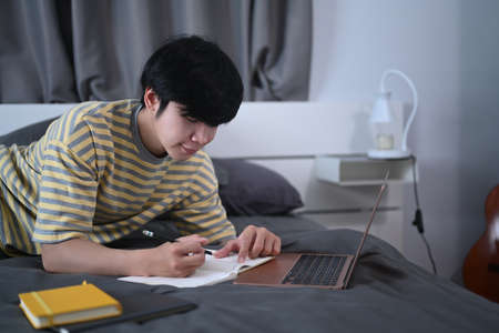 Smiling man sitting in bed and watching something on laptop computer.の写真素材
