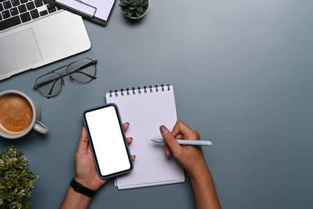 Overhead view woman holding smart phone and making notes on notebook.の写真素材