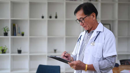 Mature doctor in white uniform working in medical office.の写真素材