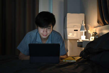Smiling man using digital tablet while sitting in bed at night.の写真素材