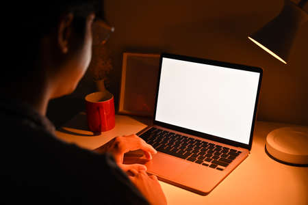 Rear view young man working online with laptop at late night.の写真素材
