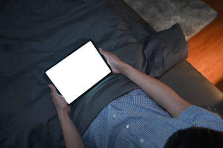 Smiling asian man using digital tablet at night in bed room.の写真素材