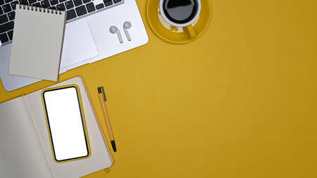 Mock up mobile phone, laptop, coffee cup and notebook on yellow background.の写真素材