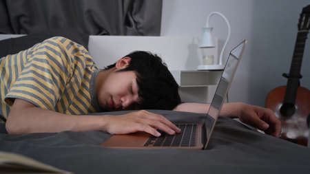Tired young asian man sleeping on bed near computer laptop.の写真素材
