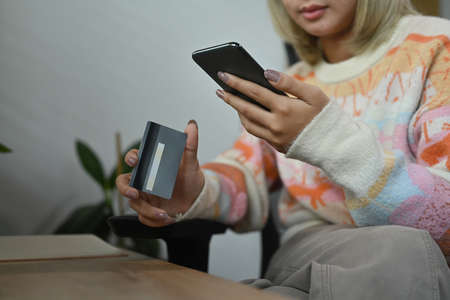 Asian woman holding credit card and shopping online with smart phone at home.