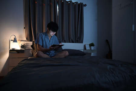 Young asian man watching movies on digital tablet at night.の写真素材