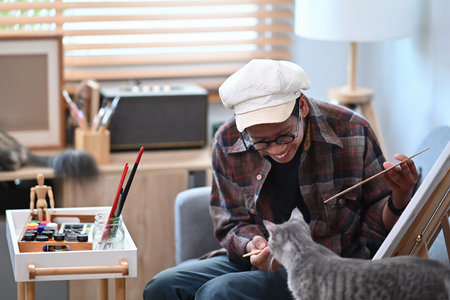 Asian man artist sitting in front of the canvas in living room and painting with water color.の写真素材