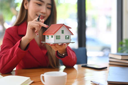Smiling asian woman holding small house model. Mortgage and real estate investment concept.の写真素材