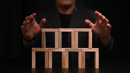 Businessman hand trying to stop dominoes. Protection finance from domino effect concept.の写真素材