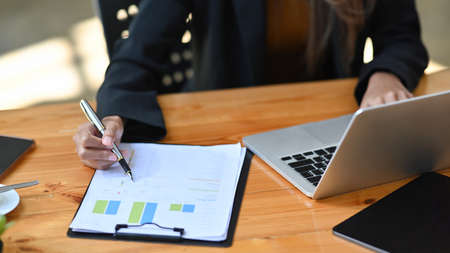 Cropped shot businesswoman using laptop computer and checking financial reports.