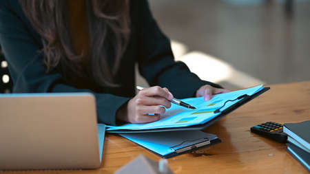 Businesswoman sitting in front of laptop and analyzing financial graphs at office desk.