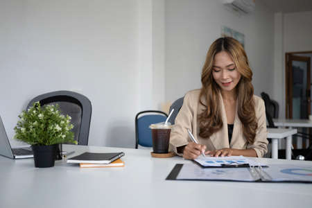 Businesswoman typing on laptop and writing information on document.の写真素材