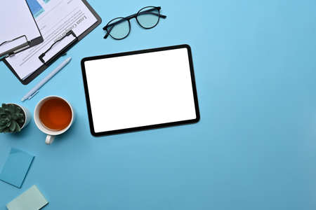 Mock up digital tablet, glasses, coffee cup and notebook on blue background.の写真素材