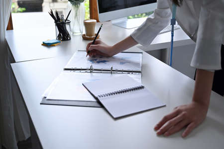 Business woman standing at her offie desk and checking financial reports.