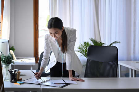 Business woman standing at her offie desk and checking financial reports.の写真素材
