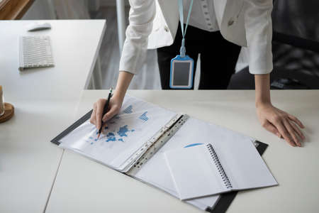 Business woman standing at her offie desk and checking financial reports.