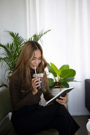 Beautiful asian woman sitting on comfortable chair in living room and writing her diary.の写真素材