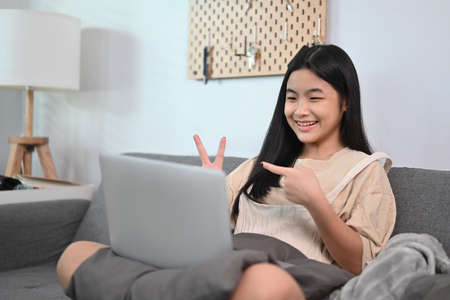 Smiling young woman sitting on sofa and having video call with computer laptop.
