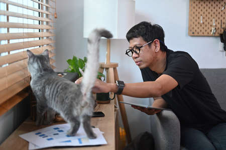 Young man relaxing inlacing room and playing with his cat.の写真素材
