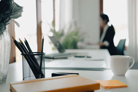 Pencil holder, book and cup of coffee on white office desk.の写真素材