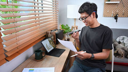 Smiling young man talking on smart phone and working with computer tablet at home.